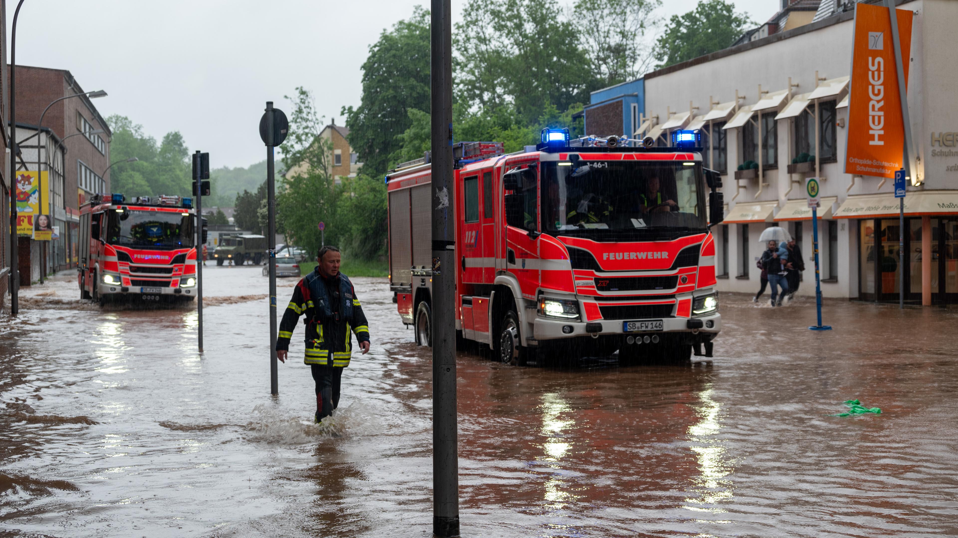 Feuerwehrleute bewegen sich und ihre LKW durch das Hochwasser in der Fischbachstraße in Saarbrücken. Nach starken Regenfällen steht diese teilweise unter Wasser. 