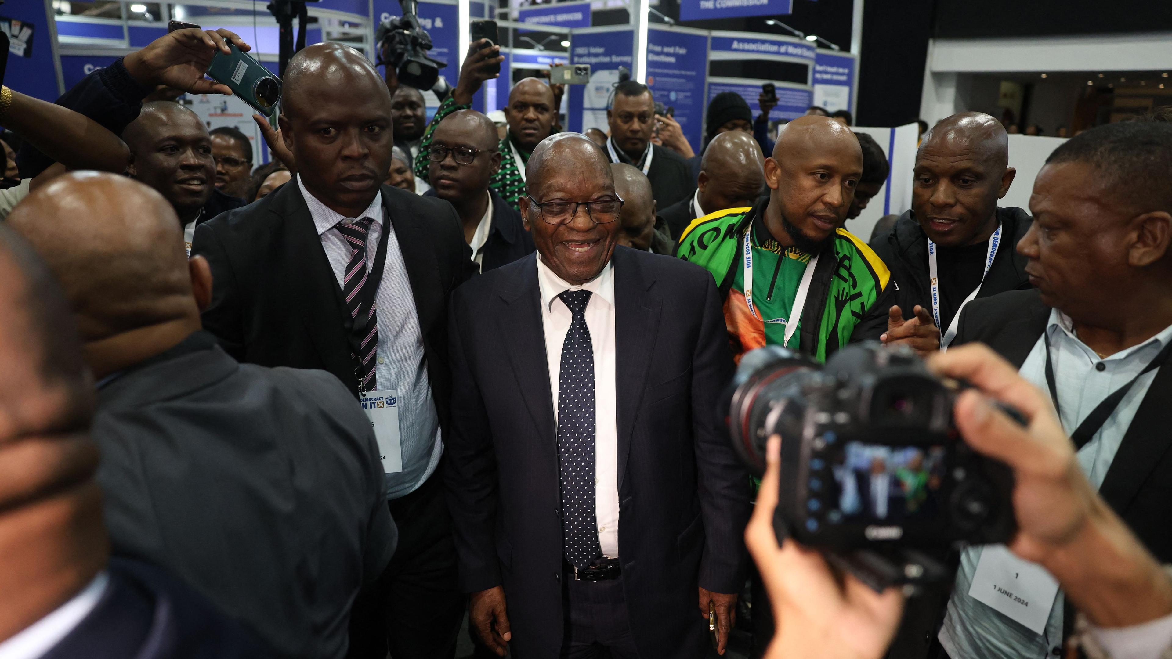 Der ehemalige südafrikanische Präsident und Führer der uMkhonto weSizwe (MK)-Partei Jacob Zuma (m.) lächelt, als er am 1. Juni 2024 im Nationalen Ergebniszentrum der Unabhängigen Wahlkommission (IEC) in Midrand eintrifft.