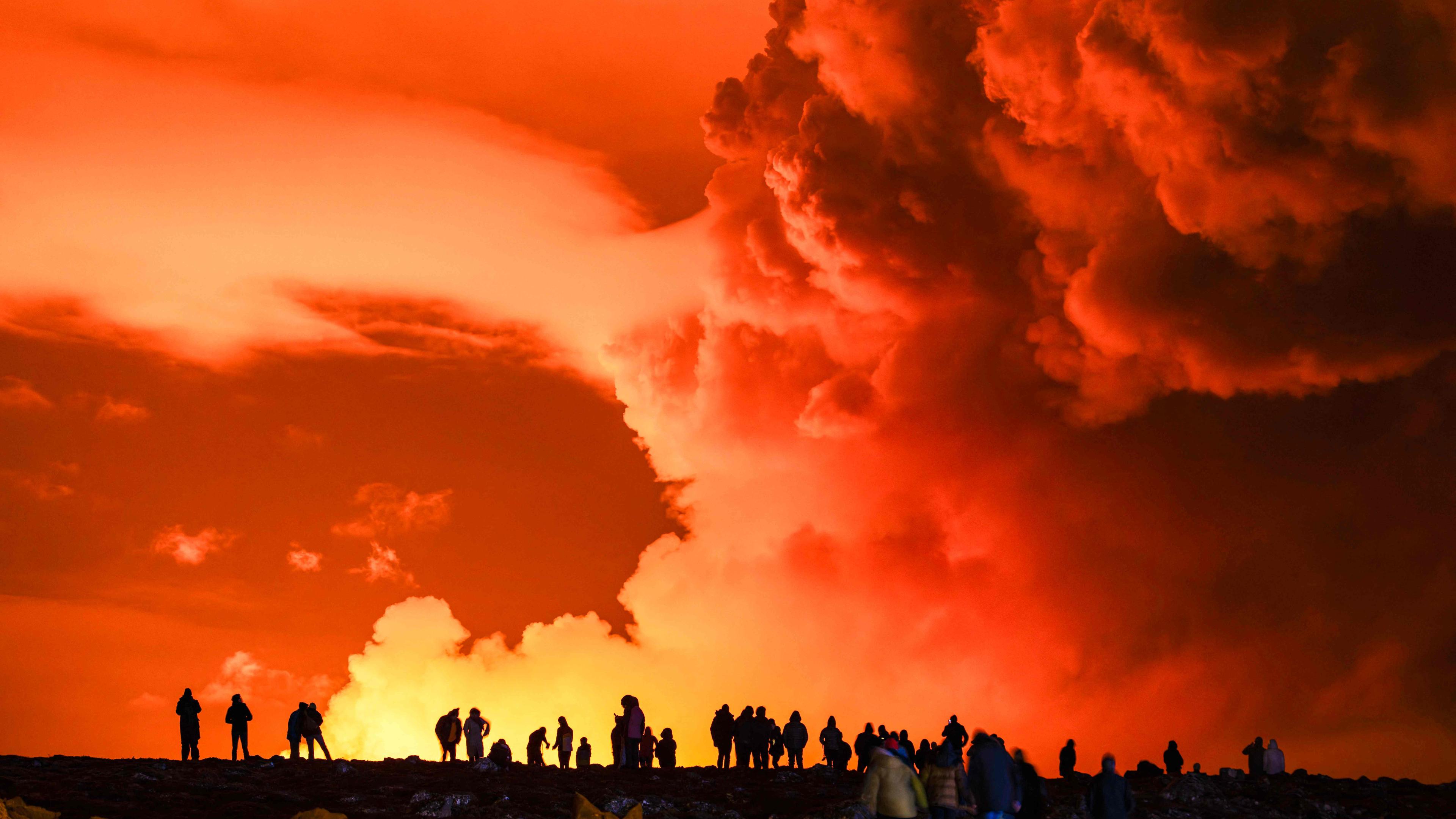(FILES) People gather to watch as molten lava flows out from a fissure on the Reykjanes peninsula north of the evacuated town of Grindavik, western Iceland on March 16, 2024. A new volcanic eruption is expected at any moment on the Reykjanes peninsula in southwestern Iceland, the Icelandic Metereological Office said on May 29, 2024, prompting authorities to again evacuate the lava-hit town of Grindavik. (Photo by Ael Kermarec / AFP)