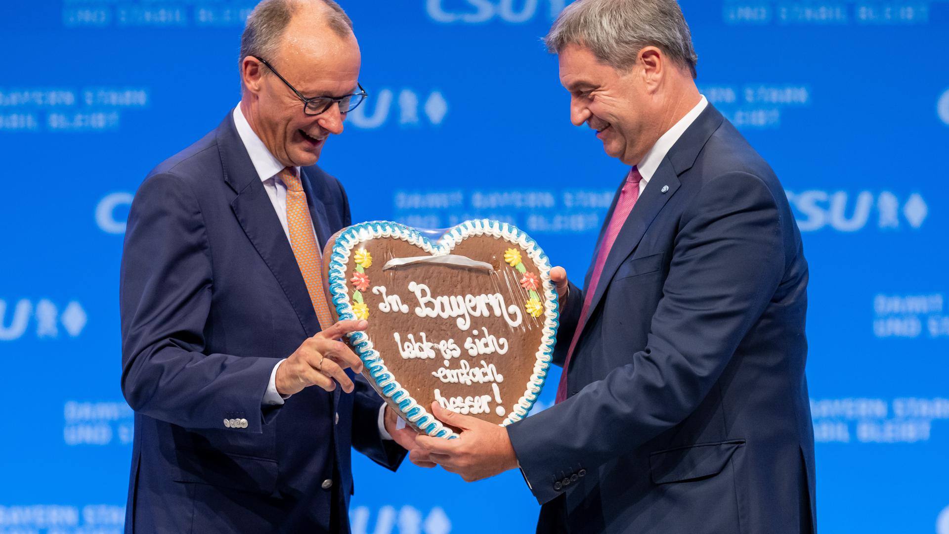 Friedrich Merz (l.), CDU-Vorsitzender, bekommt auf dem Parteitag der CSU von Markus Söder, CSU-Parteivorsitzender, ein Lebkuchenherz mit der Aufschrift „In Bayern lebt es sich einfach besser!“ geschenkt. 