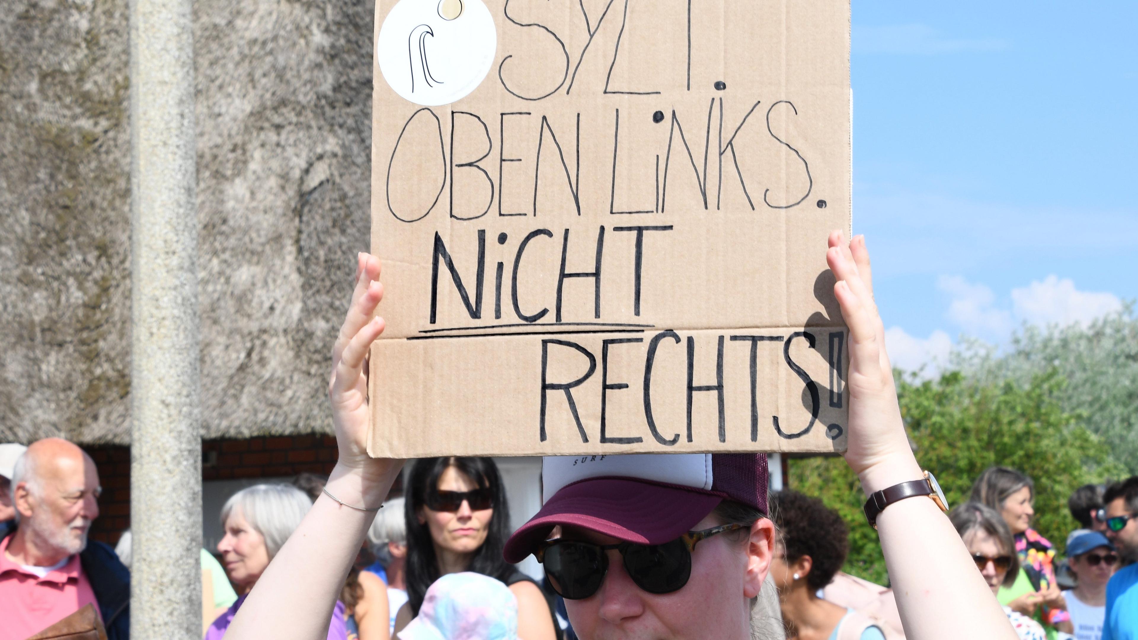„Sylt oben links nicht rechts“ steht auf einem Plakat, dass eine Frau bei einer Mahnwache am Sonntag auf Sylt in der Hand hält.