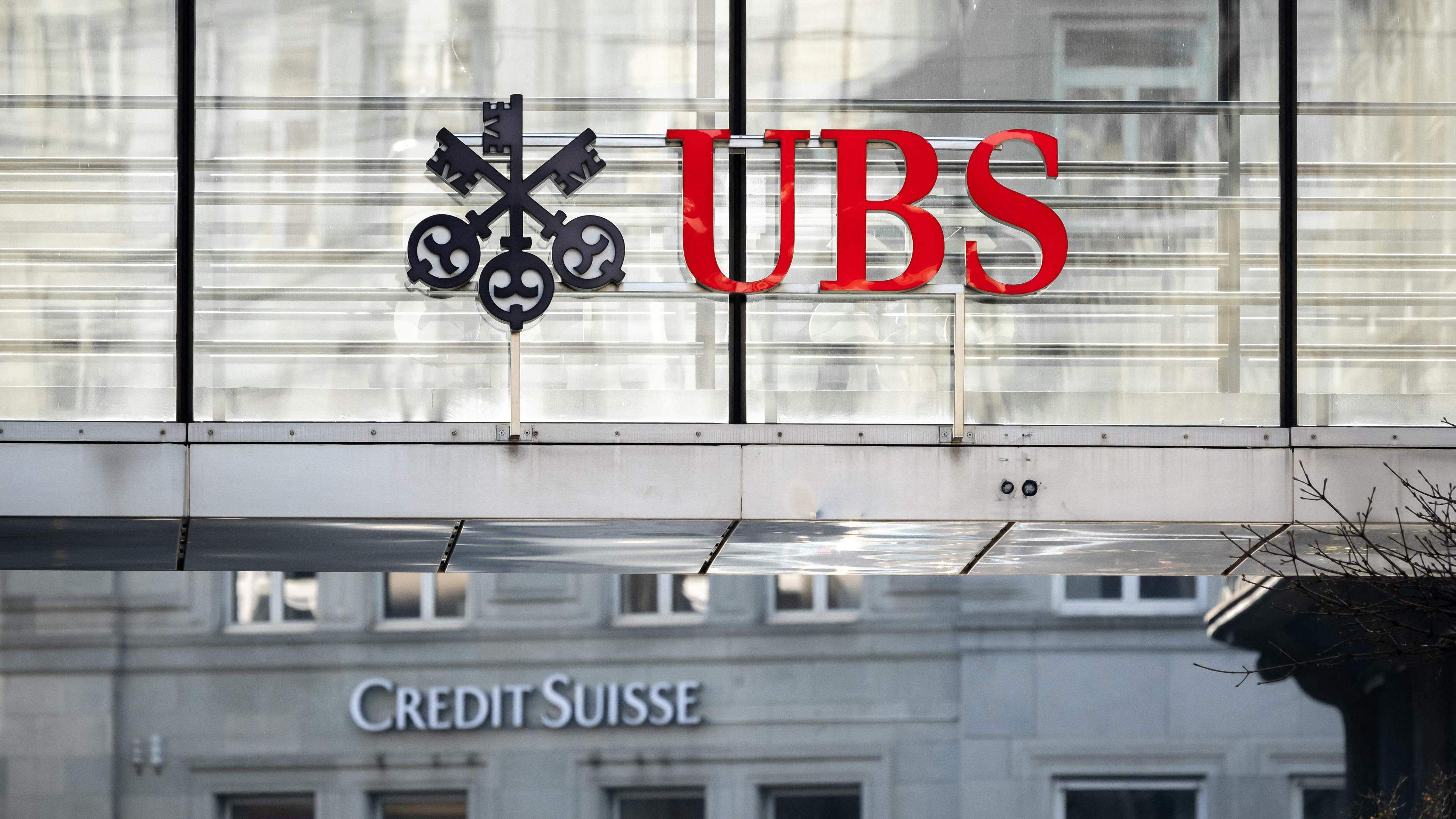 A sign and logo of Credit Suisse bank is seen beneath a sign of Swiss giant banking UBS in Zurich on March 20, 2023. - Shares in European banks sank on March 20, 2022 despite a buyout of Credit Suisse by Swiss lender UBS aimed at preventing a global banking crisis. (Photo by Fabrice COFFRINI / AFP)